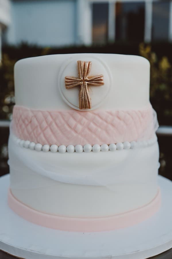 A two-tier cake covered in smooth white fondant, with a quilted pink fondant band and a piped pearl border
